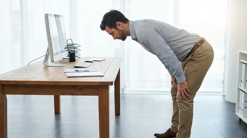 Person macht einen stehenden Hip-Hinge vor dem Schreibtisch